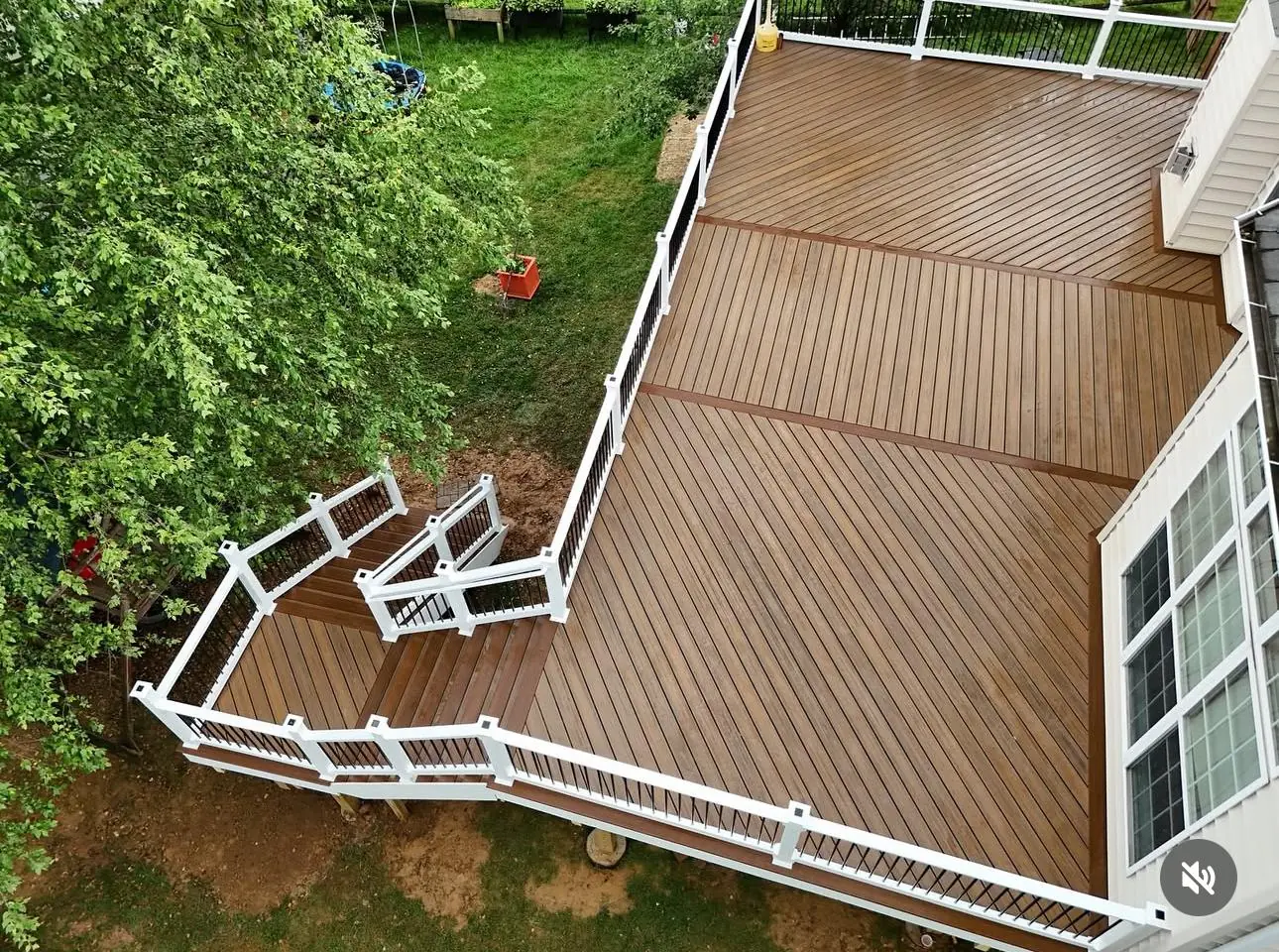 Large composite deck with wrap-around stairs and white vinyl railing posts in wooded backyard